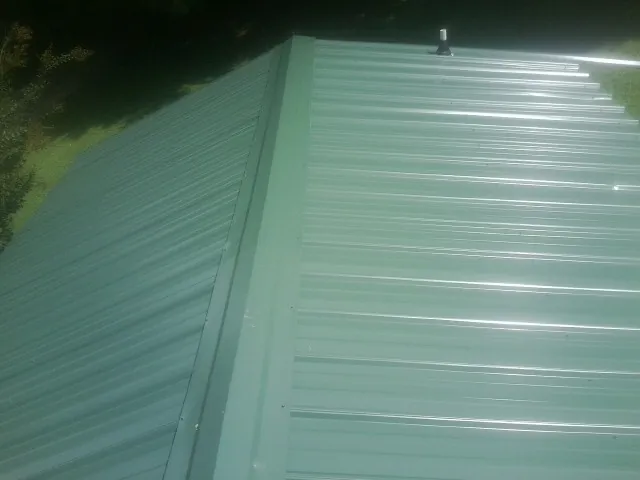 New green metal panels meeting at the ridge of a roof — Flat Roof Repair work by our crew in Nashua